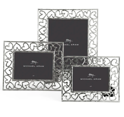 The Michael Aram Heart Frame Collection includes three silver frames with heart-shaped cutouts, each featuring a central placeholder with the brand logo—a tribute to handcraftsmanship and love.