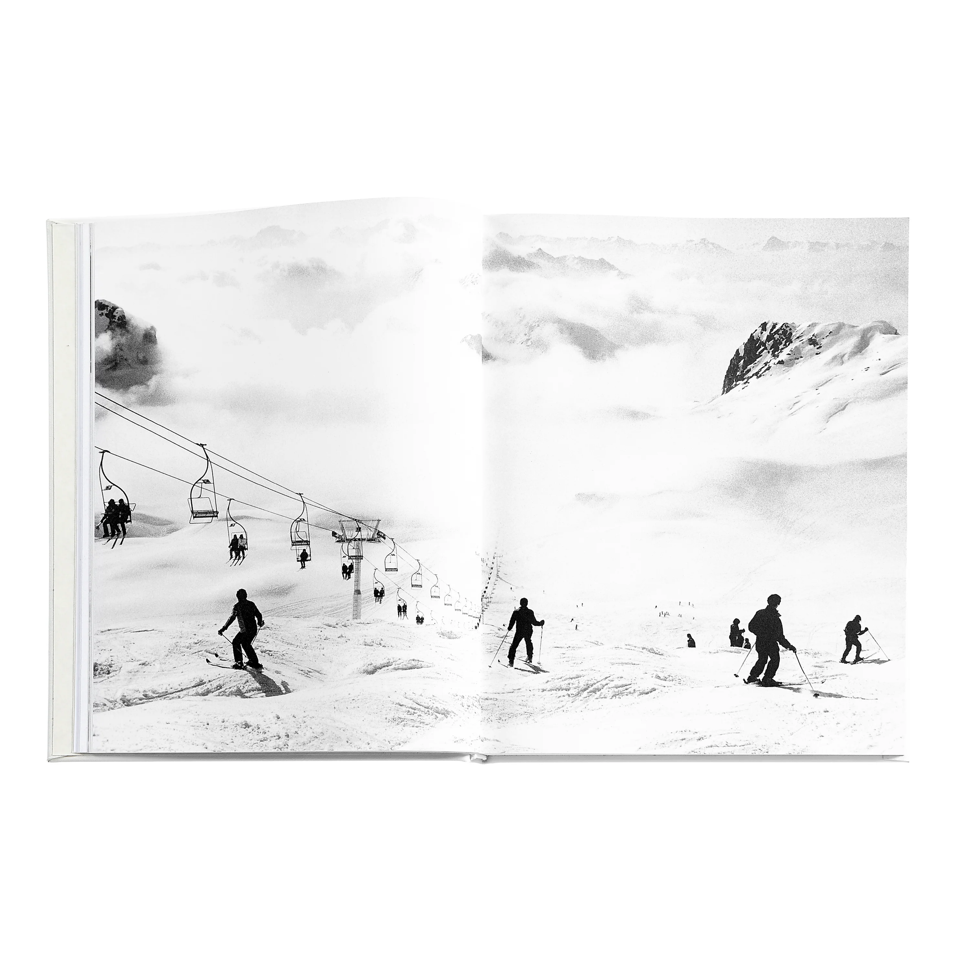 Black and white photo of skiers on a snowy slope with ski lift and distant peaks—an iconic scene from "The Ultimate Ski Book" by Graphic Image, capturing the essence of classic ski culture.