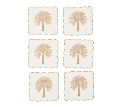 The Date Palm Cocktail Napkin Set by Kim Seybert features gold beaded palm trees on white—stylish hostess gifts and a chic match for your coastal décor.
