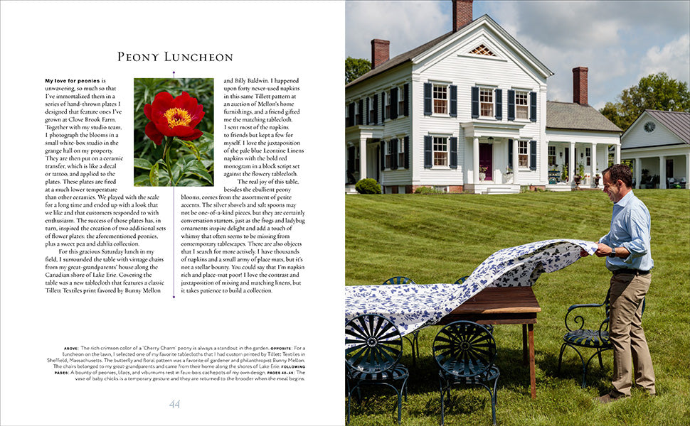 A man spreads a floral tablecloth on an outdoor dining table in front of a white historic house at Clove Brook Farm, the picturesque country retreat featured in A Year at Clove Brook Farm by Common Ground. The left page displays a peony flower and text about a peony-themed luncheon.
