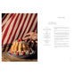 A hand decorates a Bundt-style cake adorned with raspberries and flowers on a patterned plate, set against a red and white striped background reminiscent of eighteenth-century wallpaper, with the recipe for Savoy Cake visible in A Year in the French Style by Penguin Random House.