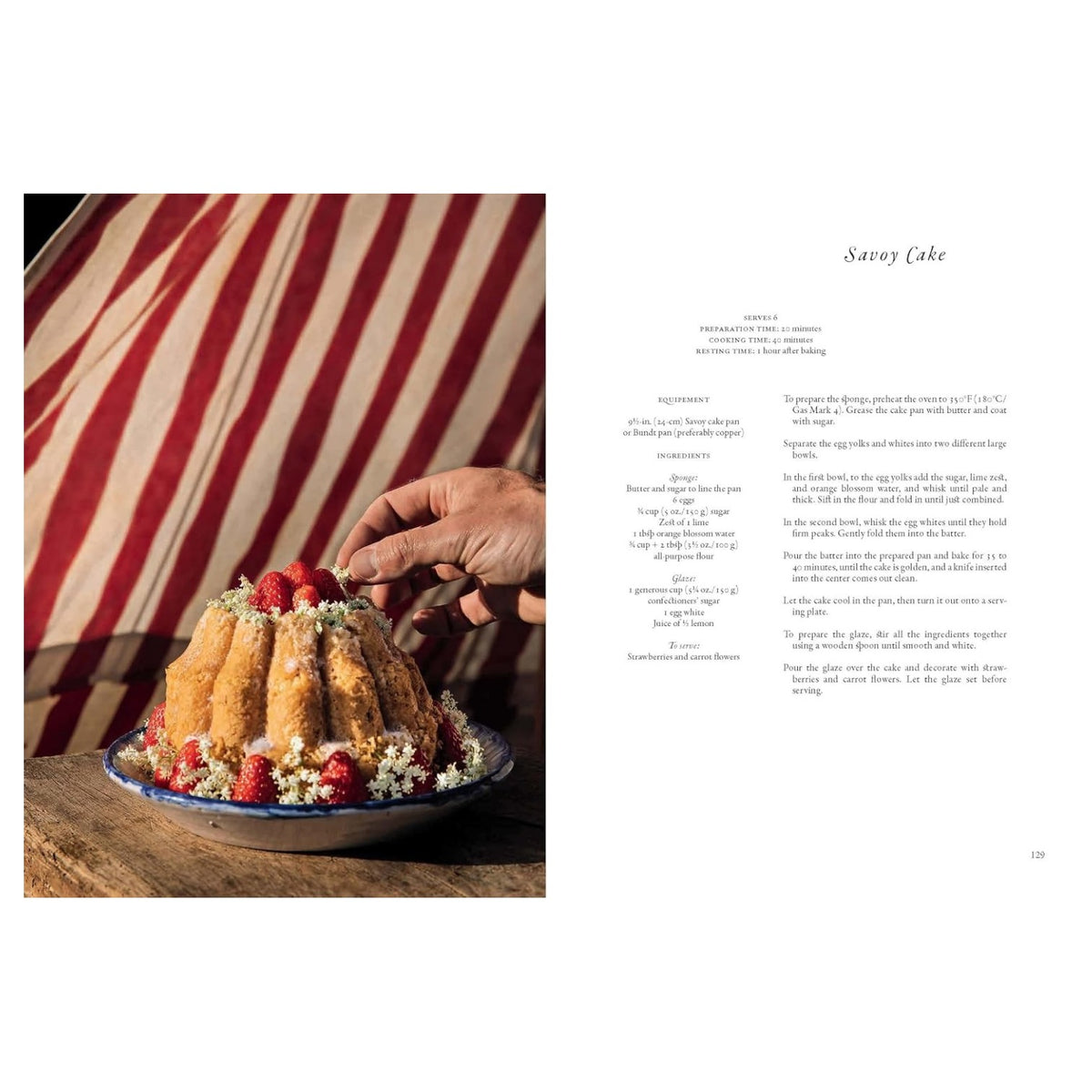 A hand decorates a Bundt-style cake adorned with raspberries and flowers on a patterned plate, set against a red and white striped background reminiscent of eighteenth-century wallpaper, with the recipe for Savoy Cake visible in A Year in the French Style by Penguin Random House.