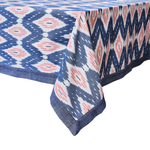 The Juliska Ikat Tablecloth features a blue, white, and pink geometric design with a dark blue border and delicate hand-stitched trim.