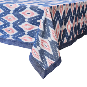 The Juliska Ikat Tablecloth features a blue, white, and pink geometric design with a dark blue border and delicate hand-stitched trim.