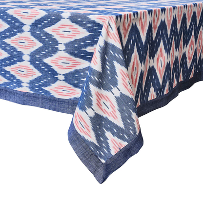 The Juliska Ikat Tablecloth features a blue, white, and pink geometric design with a dark blue border and delicate hand-stitched trim.