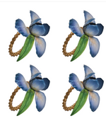 The Juliska Meadow Walk Iris Napkin Ring Set includes four identical hand-painted rings with blue and purple flowers, green leaves, and twisted gold bands—ideal for a spring tablescape.