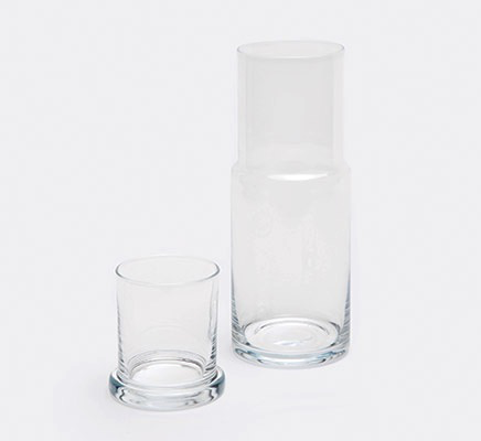 The Faro Clear Carafe by Pigeon & Poodle is placed beside an empty clear glass tumbler on a plain white background, embodying timeless hospitality.