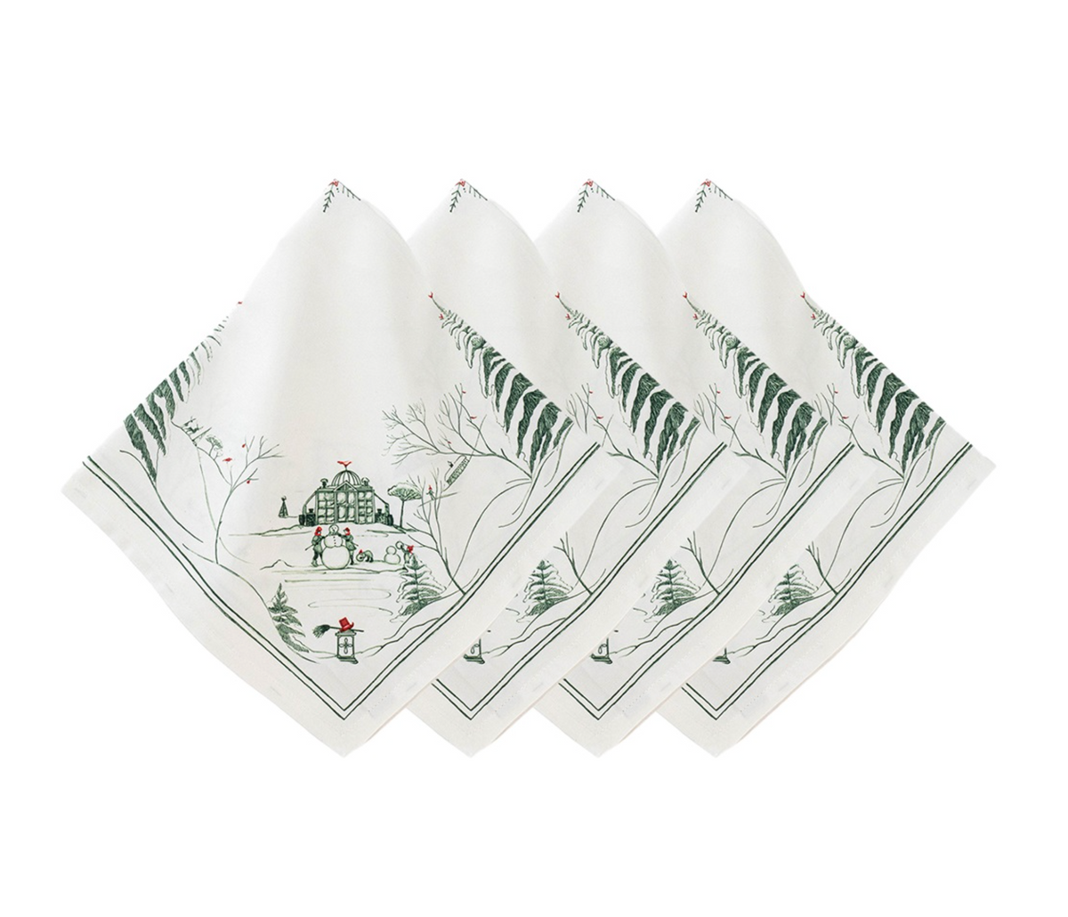 Four Juliska Evergreen Country Estate Winter Frolic napkins folded in a row, each featuring a green-ink illustration of a winter landscape with a building, pine trees, and people building a snowman.