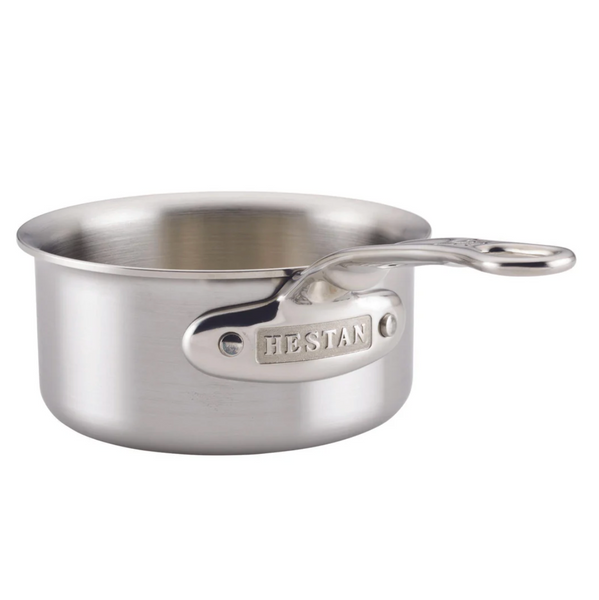 The Hestan Thomas Keller Commercial Clad Stainless Steel Butter Warmer features a tri-ply design and ergonomic handle, embossed with "HESTAN," ideal for warming butter.