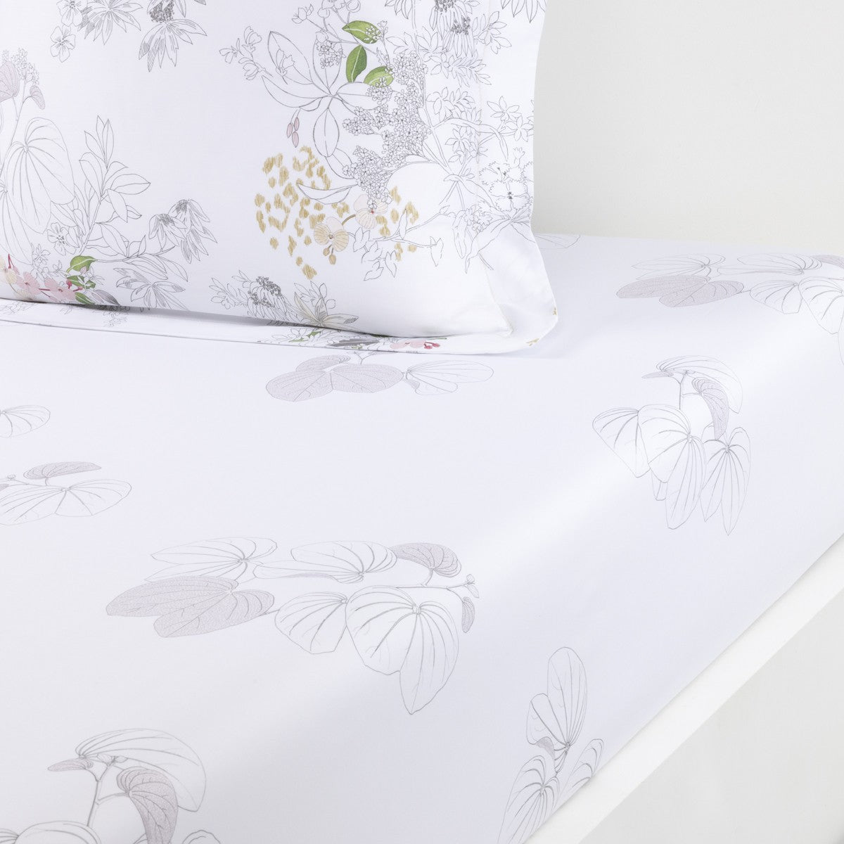 The Orchidee Bedding Collection by Yves Delorme features a white organic cotton sateen bedsheet and pillowcase with light gray, subtle botanical and floral patterns—ideal for a French bed set.