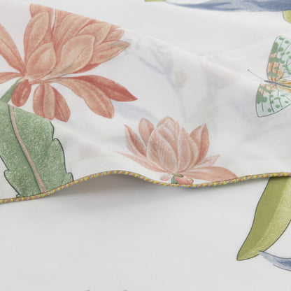 Close-up of Yves Delorme's Eze Bedding Collection showing white organic cotton bed linen with a vibrant floral print—pink flowers, green leaves—and multicolored edge stitching.