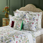 Yves Delorme Botanic Bedding Collection featuring white linens with a colorful print of flowers, butterflies, and insects, styled with coordinating shams and a square accent pillow.