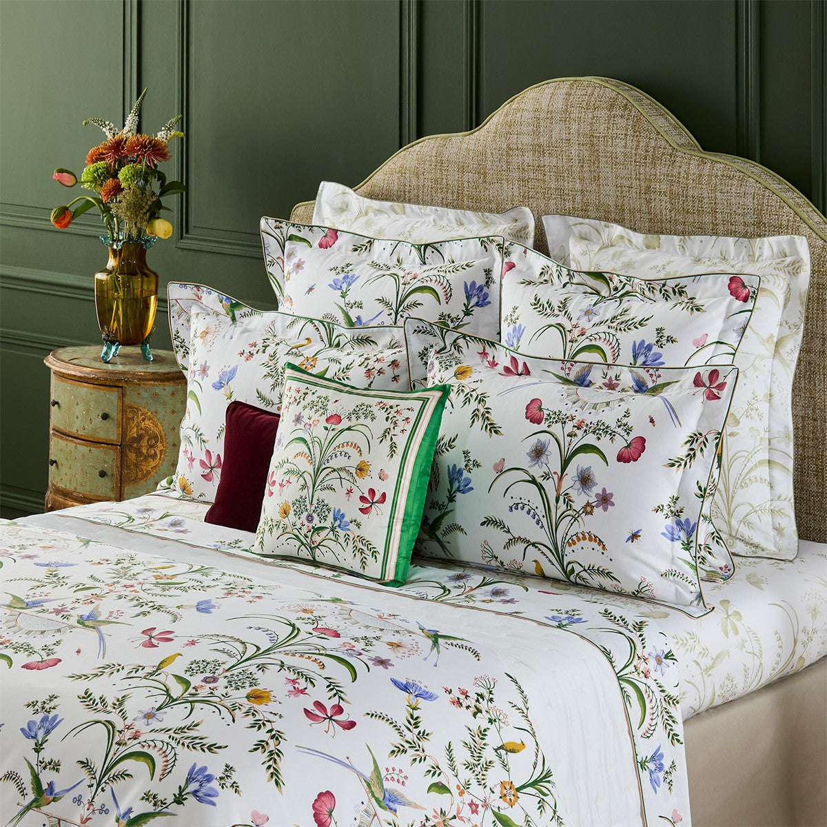 Yves Delorme Botanic Bedding Collection featuring white linens with a colorful print of flowers, butterflies, and insects, styled with coordinating shams and a square accent pillow.