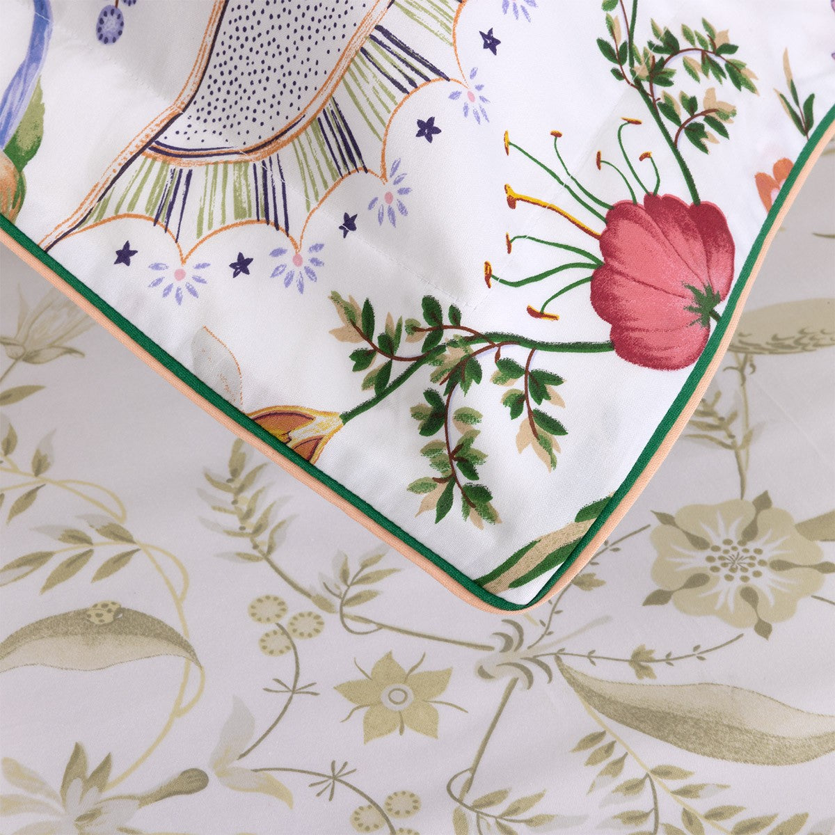 Close-up of a Botanic Bedding Collection pillow sham in organic cotton sateen with colorful botanical embroidery, resting on a flat sheet with a muted green floral pattern.