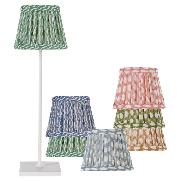 The Zafferano x Fermoie Poldina Lampshade Collection from Zafferano America includes a tall white lamp with a green patterned shade and five additional handmade pleated shades in blue, pink, green, and light green.