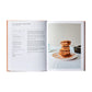 An open copy of The Italian Bakery by Phaidon shows a fig-filled spelt cookie bar recipe on the left and a photo of stacked bars on a white plate on the right.