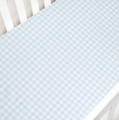 A white crib with a Gooselings Picnic Gingham Blue Crib Sheet, OEKO-TEX certified and extra soft, fitted over the mattress.