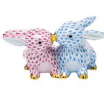 Herend's Kissing Bunnies feature two hand-painted porcelain rabbits, one pink and one blue with gold accents, sitting nose to nose.