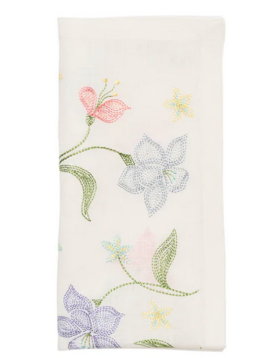 The Kim Seybert Vista Napkin Set features folded white 100% linen napkins adorned with pastel-hued sketched flowers—pink and purple petals with green stems, ideal for elegant garden parties.