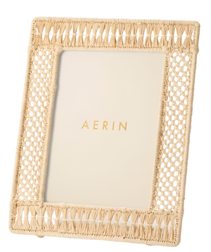 The Aerin Raffia Frame features a handwoven rattan design with a rectangular opening and displays an insert marked "AERIN" in gold, offering natural elegance to any space.