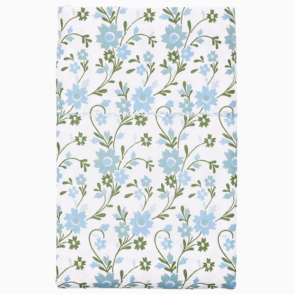 The Mihana Mist Bedding Collection by John Robshaw features folded organic cotton fabric with a white background, adorned with blue flowers and green leaves for botanical harmony.