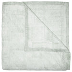 The John Robshaw Nandi Sage Coverlet is a hand-quilted, light green cotton voile coverlet with thin white and green stripes, shown folded with one corner turned over to display the underside.