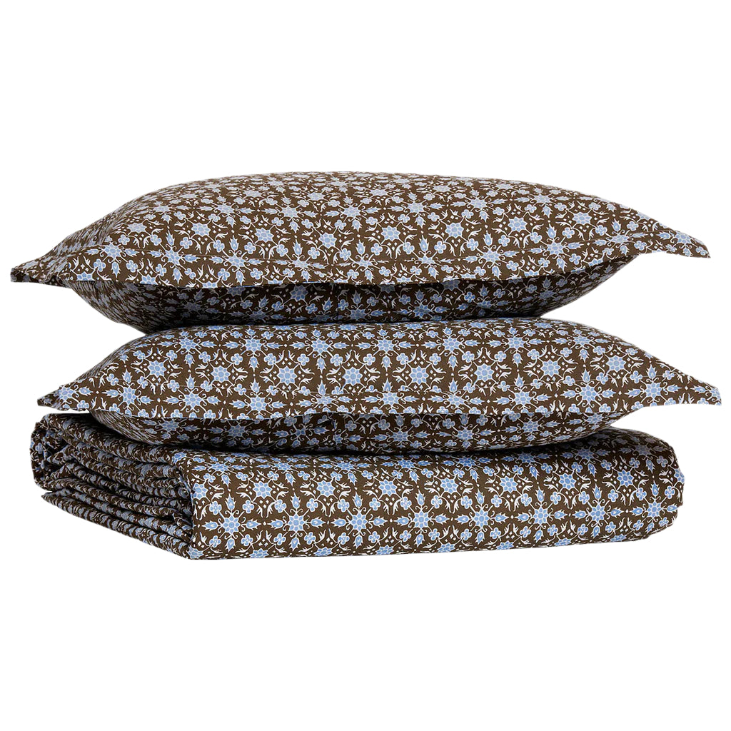 A folded Kaarik Coffee Duvet by John Robshaw, featuring a brown and blue floral pattern in organic cotton, with two matching pillowcases stacked on top.