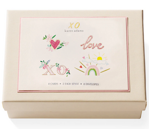 The Karen Adams XO Card Set includes a cream-colored gift box with a card on top that says “XO” and “love,” featuring hearts, rainbows, and suns. Inside are 8 hand-embellished note cards (4 styles) plus 8 envelopes.