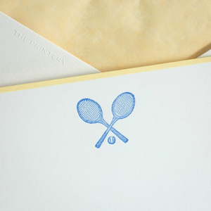 A bright white note card with a gold border and a Printery tennis racket in Ness Blue on it.
