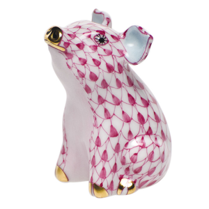 Herend's Little Pig Sitting, Raspberry Pink features a seated porcelain pig with a hand-painted pink fishnet pattern and gold accents, showcasing the brand's classic craftsmanship.