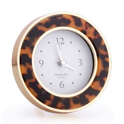 The Addison Ross Round Silver Alarm Clock features a white face with black numbers and silver hands, set in an elegant gold and tortoiseshell enamel frame—a stylish addition to any bedside table.
