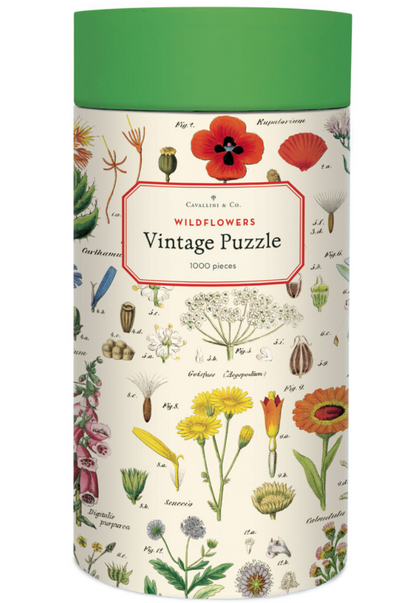 The Cavallini Papers and Co Wildflowers 1,000 Piece Puzzle comes in a cylindrical box with vintage wildflower illustrations on white, a green lid, and includes a handsewn muslin bag for storage.