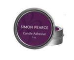 A small round metal tin labeled "Simon Pearce Candle Adhesive" sits slightly open in front of another tin—ideal for firmly securing candles to any candle base.