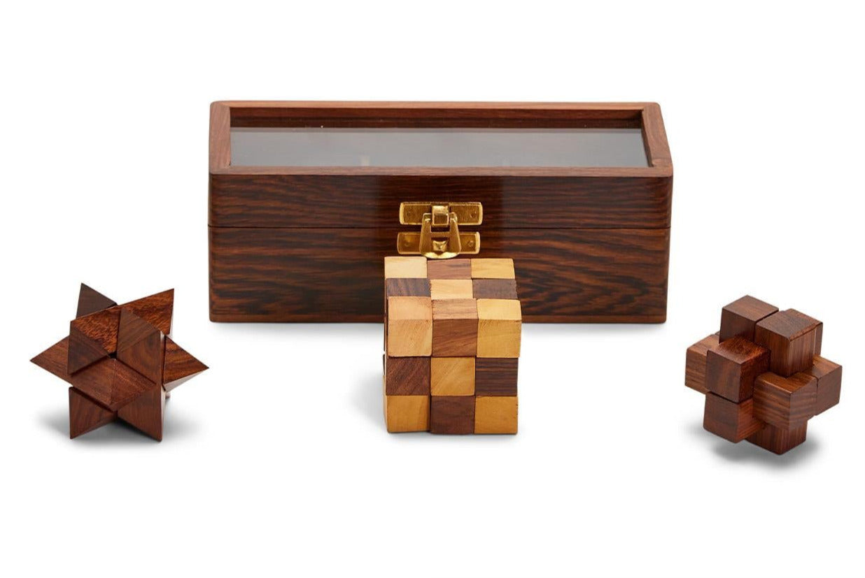 Three Turf Club Wood Crafted Puzzles by Two's Company, made of acacia wood and designed as brain teasers, are displayed in front of a rectangular wooden box with a transparent lid. Perfect for engaging visual-spatial faculties and offering hours of challenging entertainment.