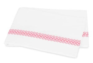 A folded white towel from the Matouk Astor Braid Bedding Collection in Peony, featuring a decorative loop pattern in pink along one edge and embroidered with timeless script.