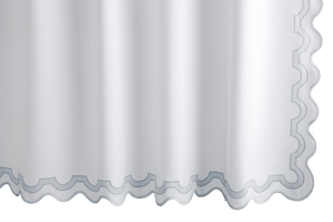 The Matouk Mirasol Shower Curtain in Pool, featuring scalloped edges and light blue trim, elegantly hangs with a blend of style and sustainability. It's crafted to meet OEKO-TEX® Standard 100 certification.
