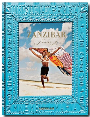 A book titled "Zanzibar" by Assouline with a vibrant blue border featuring text and an image of a person joyfully holding a colorful cloth on a sandy beach under the blue sky and clouds of the Indian Ocean.