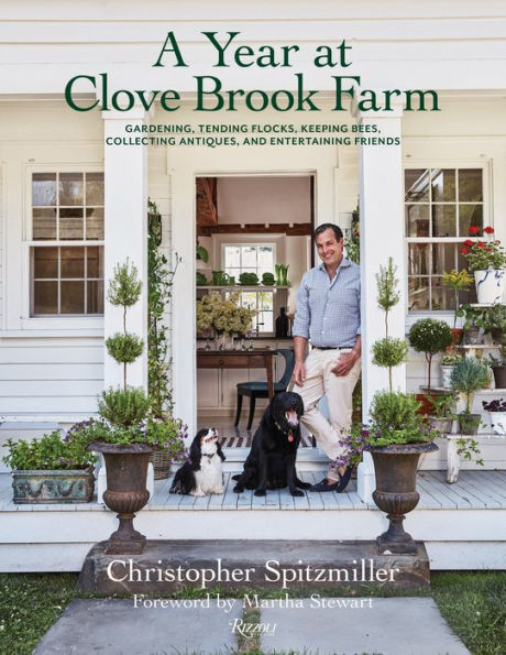 A man stands with two dogs on a charming porch surrounded by lush plants. The book "A Year at Clove Brook Farm" by Christopher Spitzmiller, from Common Ground, suggests sustainable living and seasonal entertaining in this idyllic retreat.