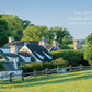 A stone farmhouse with multiple chimneys, surrounded by greenery and a wooden fence that channels Bunny Mellon's iconic garden design, is labeled "Oak Spring Garden and Farm, Upperville, Virginia," reminiscent of the style showcased in "Gardens of Bunny Mellon" by Common Ground.