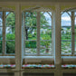 Through the three-paned window, a meticulously designed garden unfolds with trees and shrubs. Window seats feature floral-patterned cushions, echoing the elegance of Bunny Mellon from Common Ground's "Gardens of Bunny Mellon.