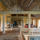 The rustic living room showcases the elegance of Pietro Cicognani: Architecture and Design by Common Ground, with wooden beams, vibrant artwork on the walls, and a seating area bathed in natural light through large windows.