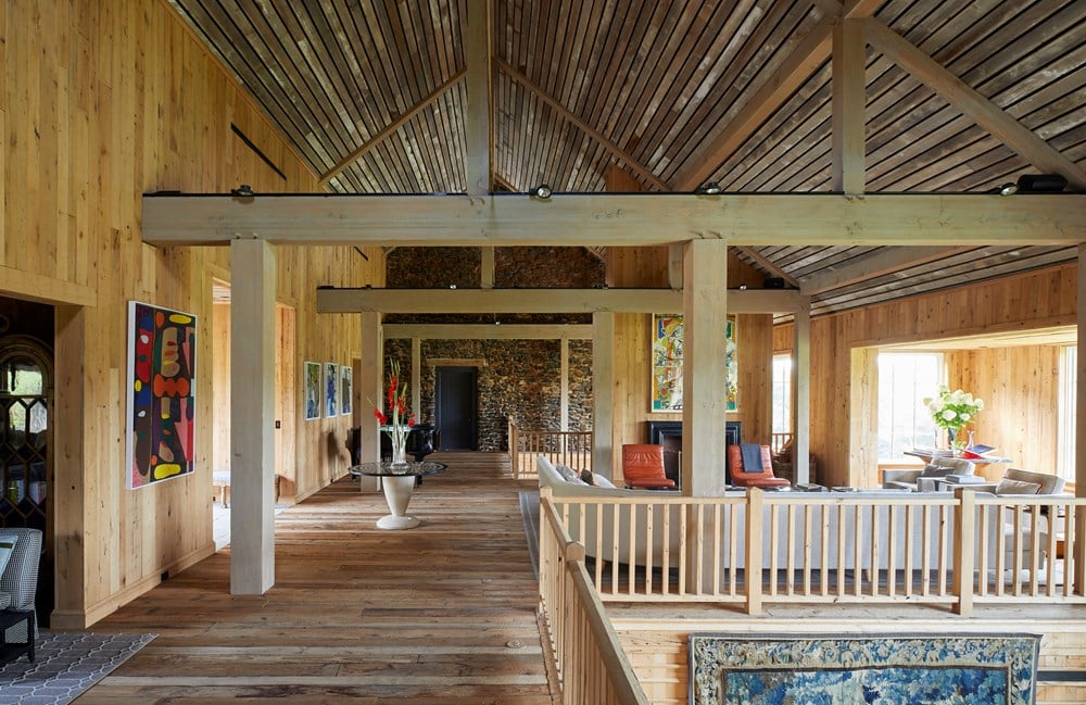 The rustic living room showcases the elegance of Pietro Cicognani: Architecture and Design by Common Ground, with wooden beams, vibrant artwork on the walls, and a seating area bathed in natural light through large windows.