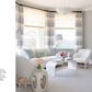 Discover elegance in "The Principles of Pretty Rooms" by Abrams, showcasing a refined interior with white and light blue decor, featuring chairs, a loveseat, side tables adorned with flowers, and large windows with striped curtains.