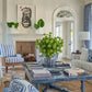 Featuring striped armchairs, a large green plant centerpiece, and abstract art above the fireplace, this elegant living room is bathed in natural light through arched windows and doors. It embodies timeless interiors highlighted in Abrams' "The Principles of Pretty Rooms.