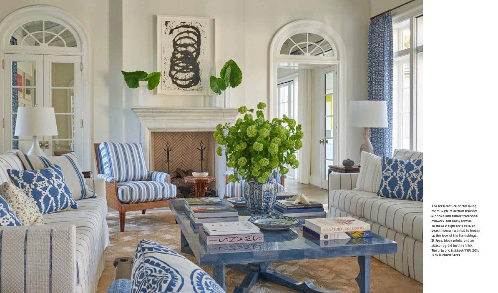 Featuring striped armchairs, a large green plant centerpiece, and abstract art above the fireplace, this elegant living room is bathed in natural light through arched windows and doors. It embodies timeless interiors highlighted in Abrams' "The Principles of Pretty Rooms.
