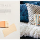 A beige-painted brush rests on a white surface near Penguin Random House’s "Living with Color," while patterned pillows and a white fur throw enhance the blue sofa, showcasing stylish home decor.