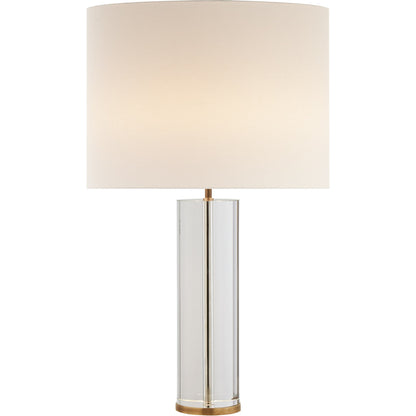 A Lineham Table Lamp by Visual Comfort with a cylindrical clear glass body, antique brass accents, and a large, round, beige lampshade.