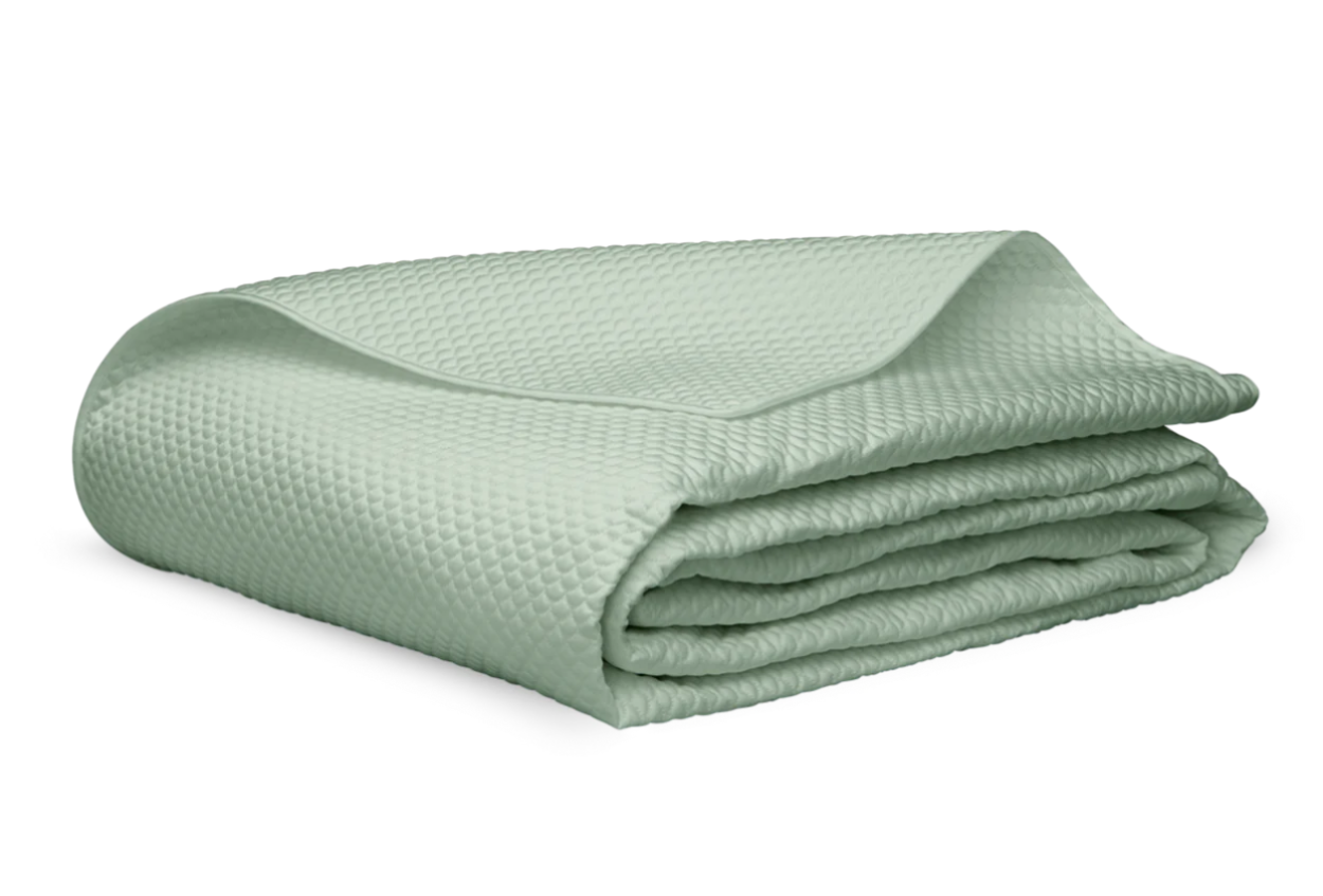The Matouk Alba Bedding Collection in Opal features a folded light green textured blanket with a raised dot pattern, crafted from OEKO-TEX® certified Egyptian cotton sateen, shown on a white background.