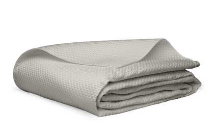 A neatly folded Alba Bedding Collection blanket in silver by Matouk, featuring a light gray textured Egyptian cotton design, is displayed on a white background.