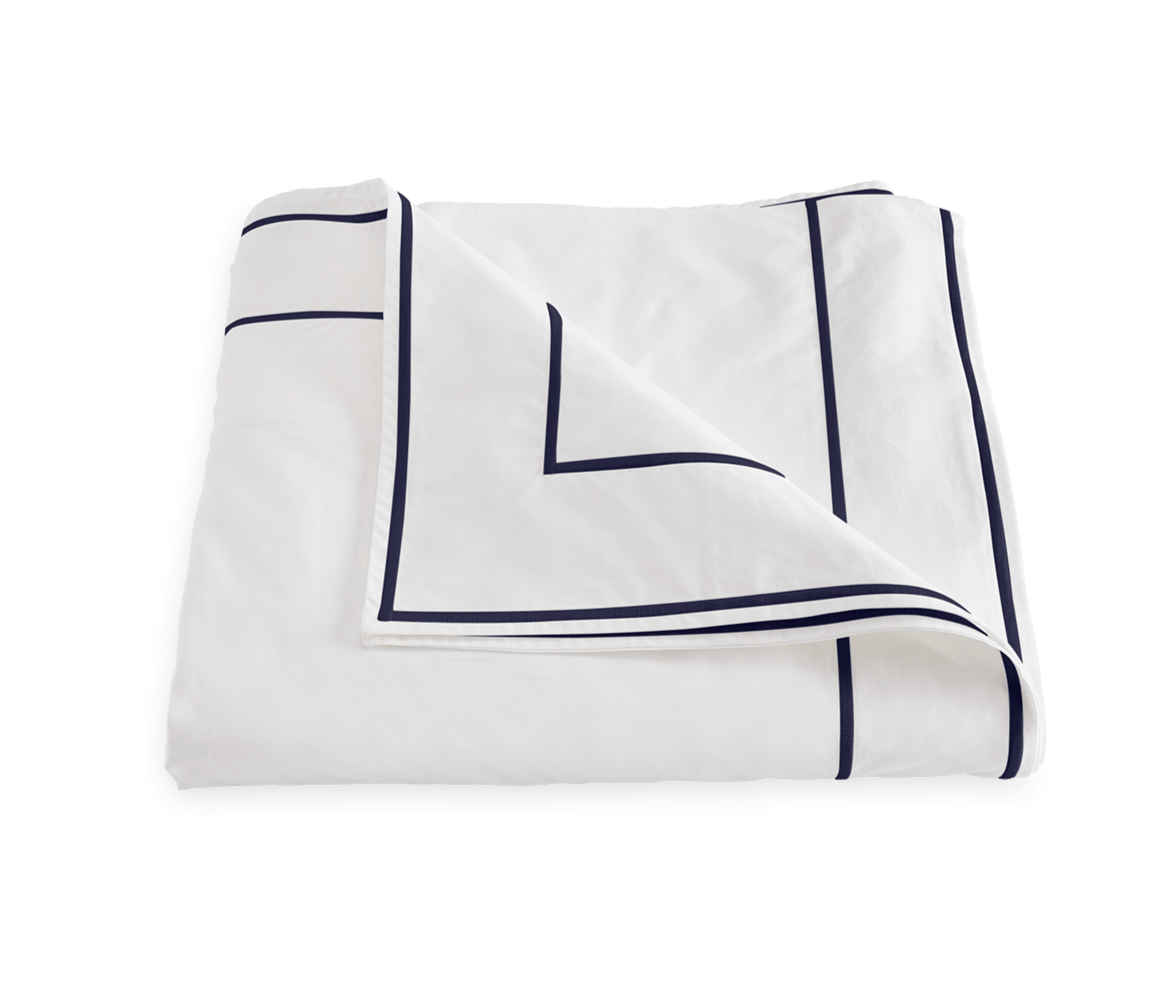 The Ansonia Bedding Collection by Matouk features a folded white Egyptian cotton percale bedsheet with a navy geometric border and satin stitching, shown against a plain background.